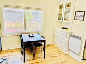 A small kitchen with a dining table, chairs, a white cabinet, and a window with a view of a wooden fence and trees.