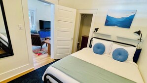 Quarto com cama, televisão num canto, quadro na parede e porta que dá para outro espaço.