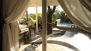 A glass door leading to a patio with a hammock, a hot tub, and a seating area with a colorful blanket.