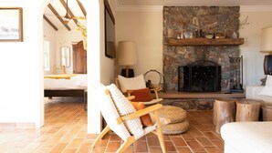 A cozy living room with a stone fireplace, a wooden chair, and a bed in the background.