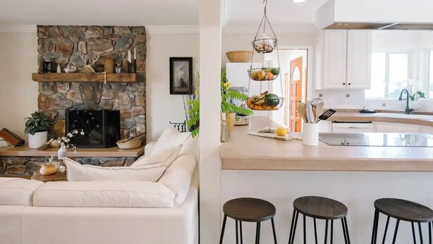 A modern living room with a stone fireplace, a white sofa, and a kitchen with a bar area.