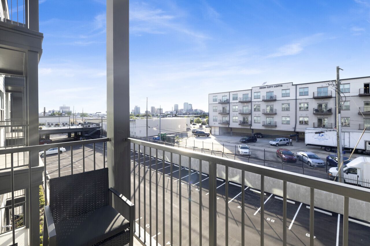 Vue depuis un balcon donnant sur un parking et un immeuble portant l’inscription « 1800 CITY LOFTS ».