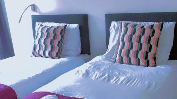 A hotel room with a large bed, two pillows with a geometric pattern, a red blanket, and a painting of flowers on the wall. - The Ridgmont-st Albans-high Street- Near Luton Airport -train Station-balcony (St Albans)