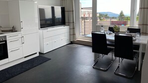 A modern kitchen with white cabinetry, a flat-screen TV, and a dining area with a table and chairs. - COZY PENTHOUSE in the middle of the BAVARIAN FOREST +NETFLIX +POOL +SAUNA +GYM (Sankt Englmar)
