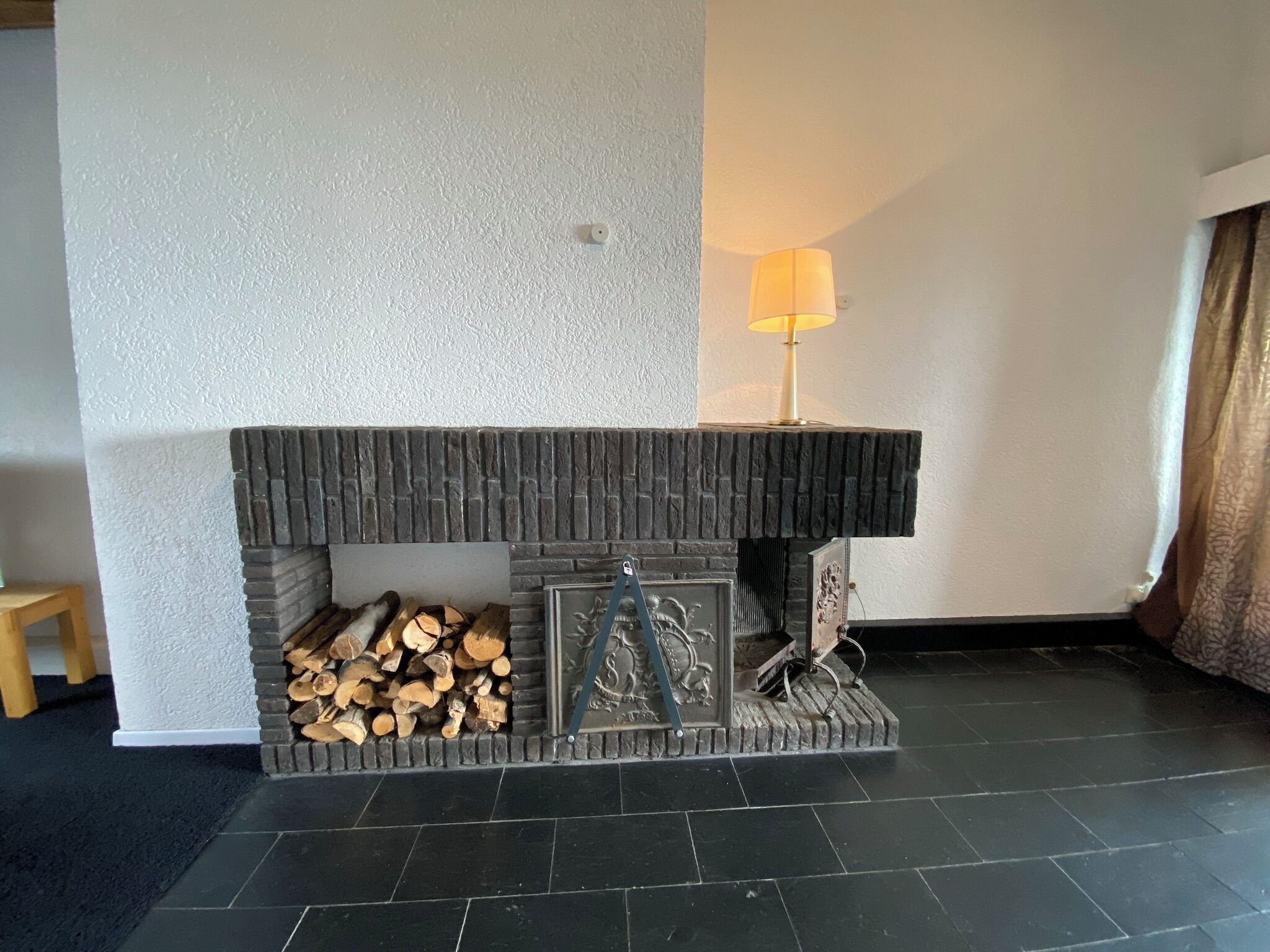 Een open haard met een stenen bovenkant, een stapel hout en een decoratief metalen object.