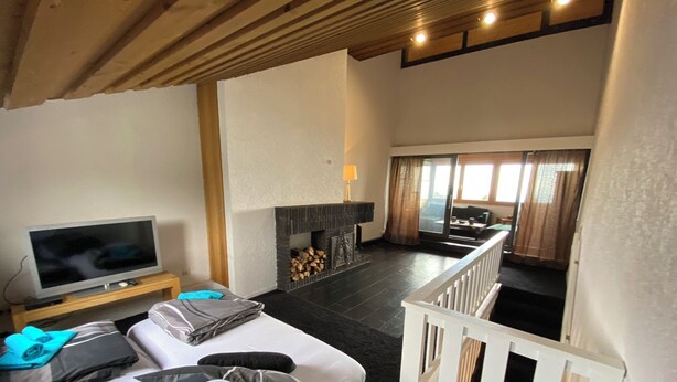 A modern living room with a flat-screen TV, a sofa with cushions, a fireplace, and a balcony with a railing. - COZY PENTHOUSE in the middle of the BAVARIAN FOREST +NETFLIX +POOL +SAUNA +GYM (Sankt Englmar)