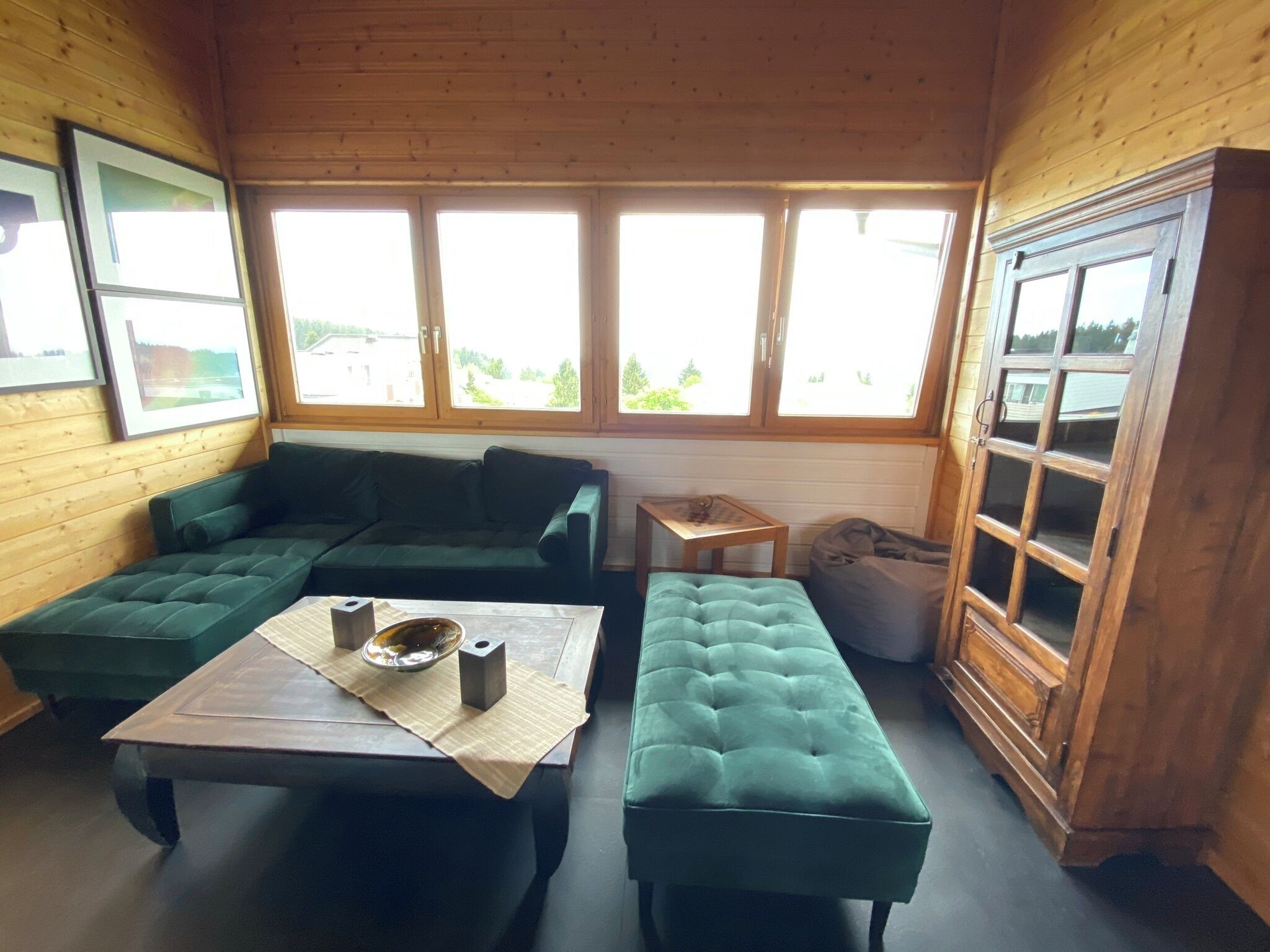 A cozy room with a green sofa, a small table with a bowl and two candles, and a window with a view of greenery.
