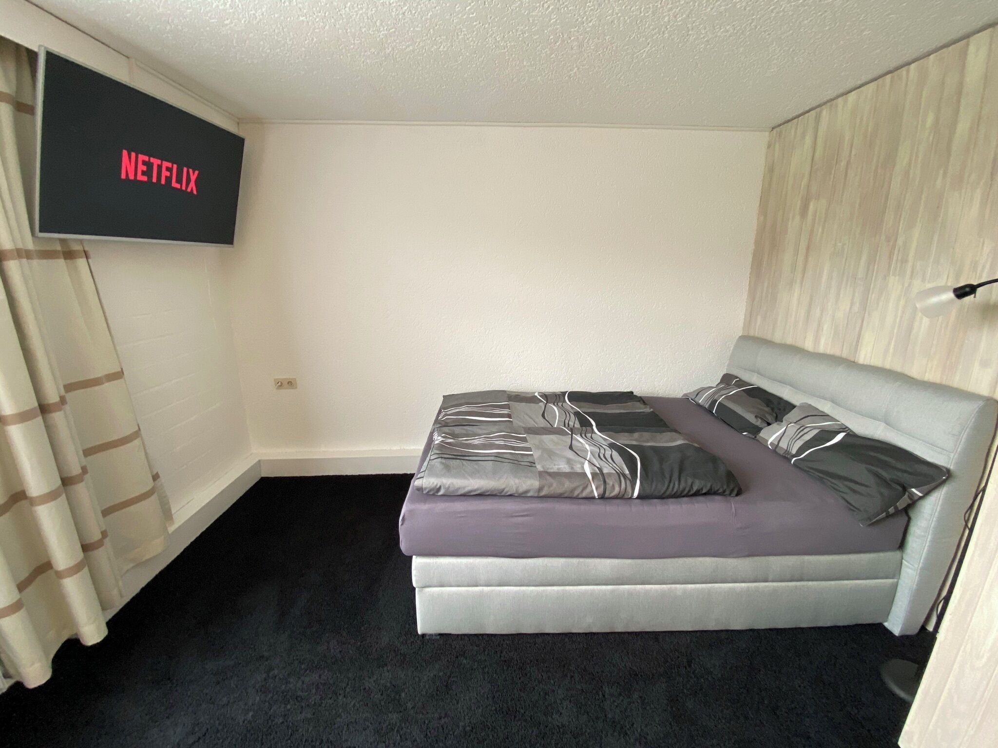A bedroom with a bed, a TV mounted on the wall, and a curtain.
