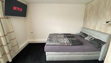 A bedroom with a bed, a TV mounted on the wall, and a curtain.