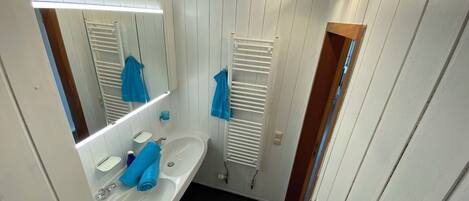 Une petite salle de bain aux dimensions réduites, avec un lavabo blanc, un miroir et un porte-serviettes.