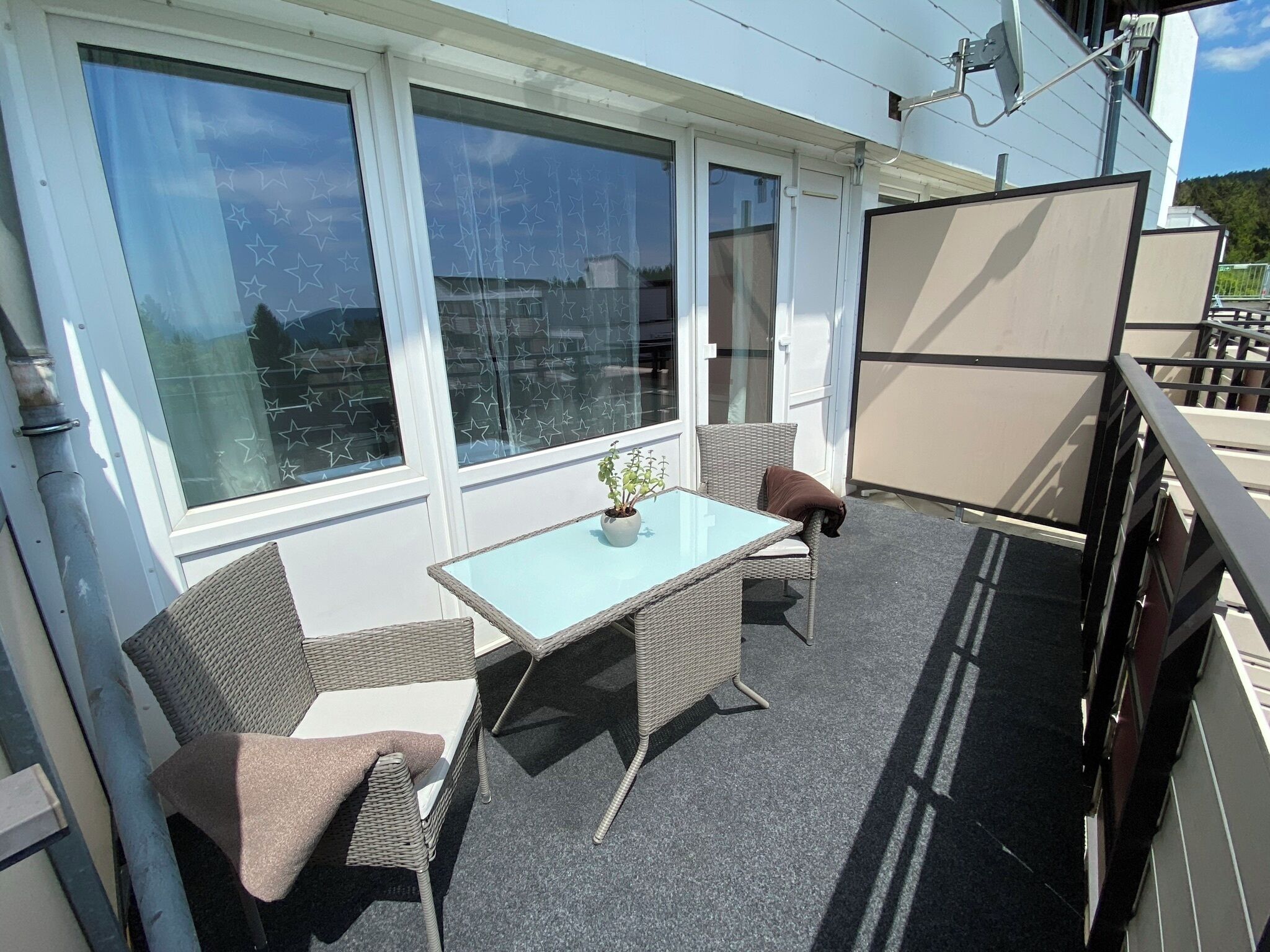 Een balkon met een glazen tafel, rieten stoelen en een bloempot.