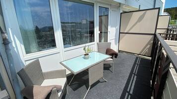 Een balkon met een glazen tafel, rieten stoelen en een bloempot.