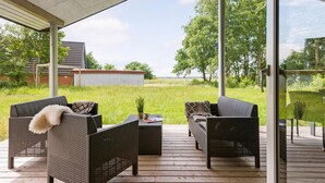 An outdoor deck with wicker furniture, a small table, and a view of a grassy field and trees. - 3 bedroom pet friendly home in ørsted (Ørsted)