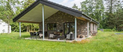Ein modernes Haus mit überdachter Terrasse, Ziegelmauern und einem großen Fenster.
