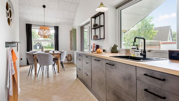 A modern kitchen with a large window, wooden cabinets, and a dining area with chairs. - 3 bedroom pet friendly home in ørsted (Ørsted)