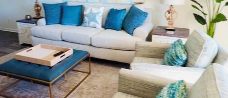 Un salon avec un canapé beige, des coussins bleus, une table basse et une grande plante.