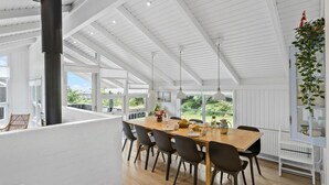 Un'ampia sala da pranzo con soffitto alto, grandi finestre e vista sul verde circostante.