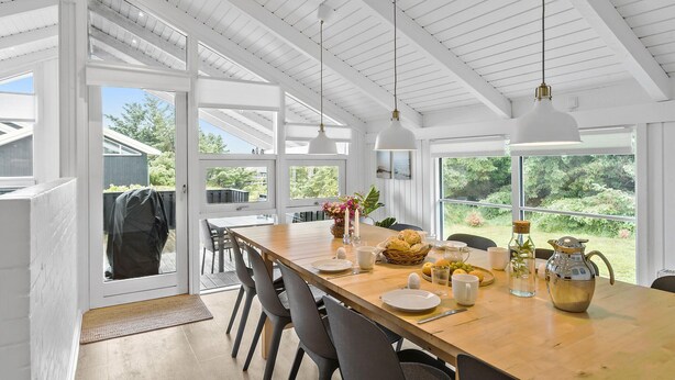 Ampia sala da pranzo con tavolo in legno apparecchiato per quattro persone, grandi finestre che offrono vista sul verde e travi a soffitto bianche.