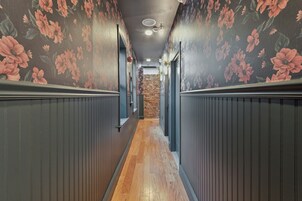 A narrow hallway with wooden flooring, flanked by dark walls with floral wallpaper.