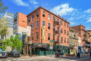 A multi-story brick building with a restaurant on the ground floor, a fire escape, and a street view with cars and pedestrians.
