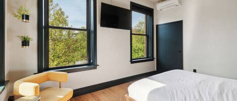 A modern bedroom with a large bed, a chair, and a TV mounted on the wall.