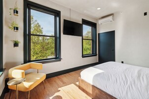 A modern bedroom with a large bed, a chair, and a TV mounted on the wall.