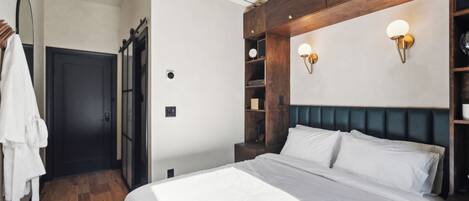 A hotel room with a bed, a wardrobe, a mirror, and a wall-mounted shelf with decorative items.