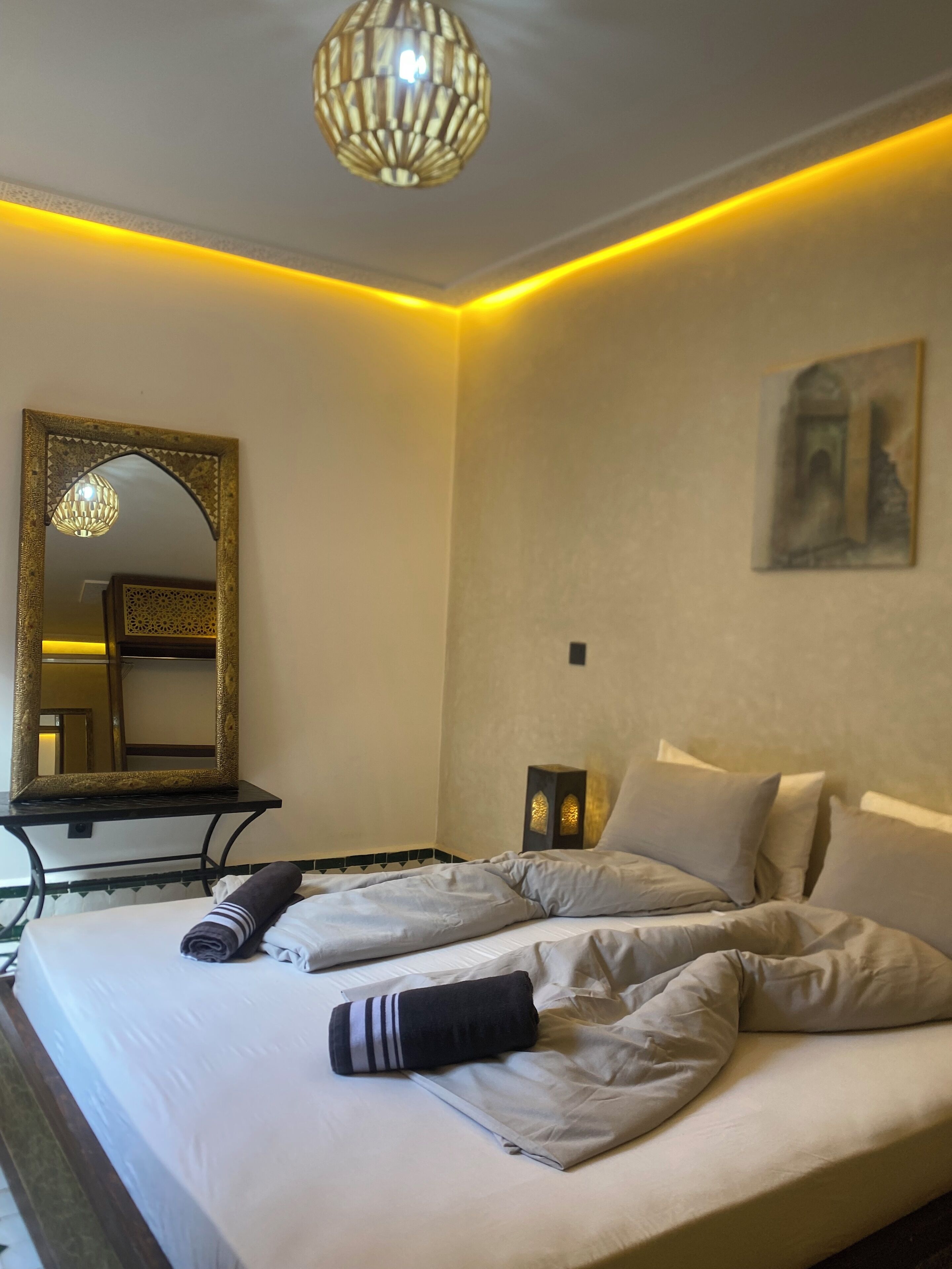A hotel room with a bed, a mirror, a wall-mounted light fixture, and a painting.