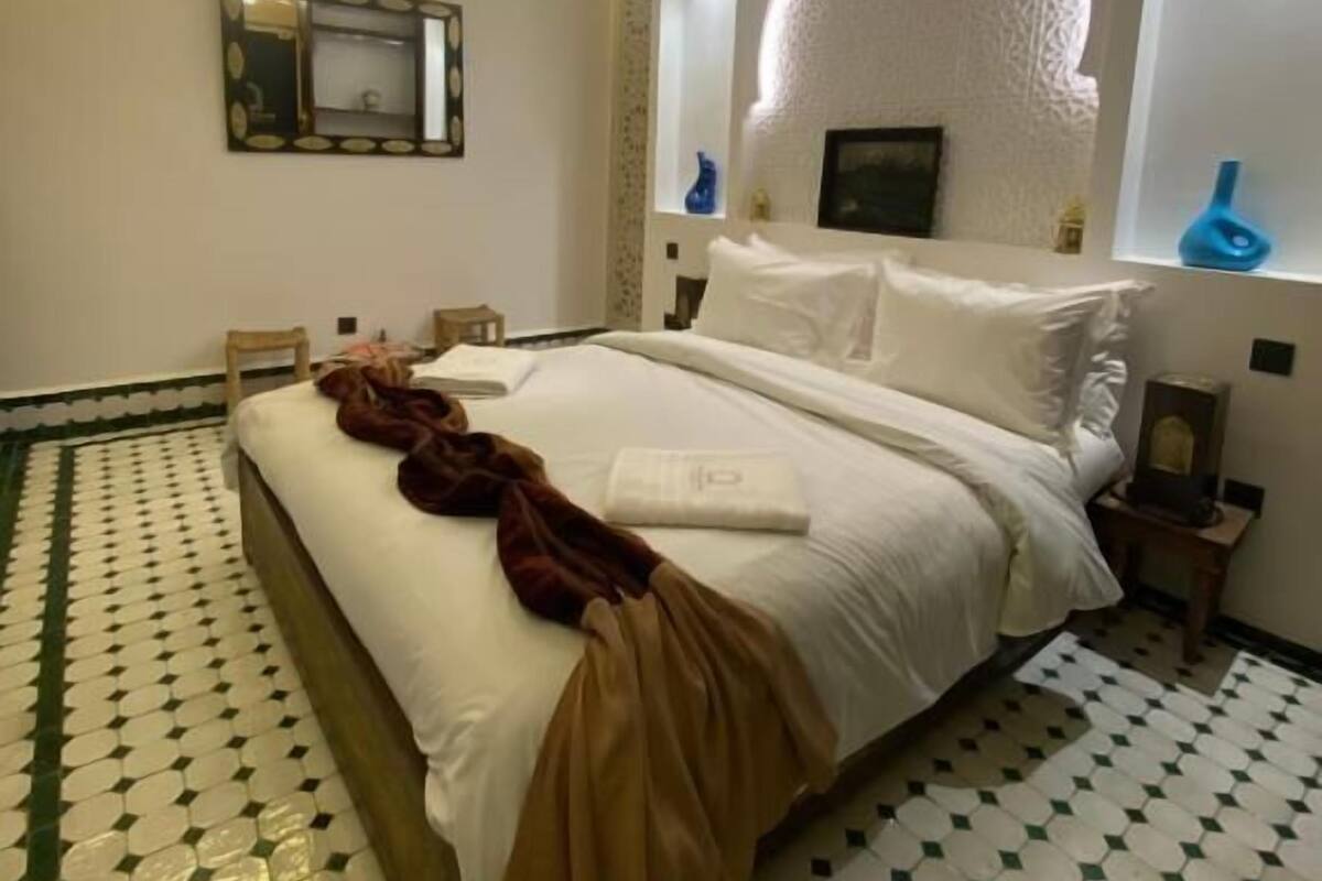 Une chambre d’hôtel avec un grand lit, un mur décoratif, un miroir et un sol à motifs.