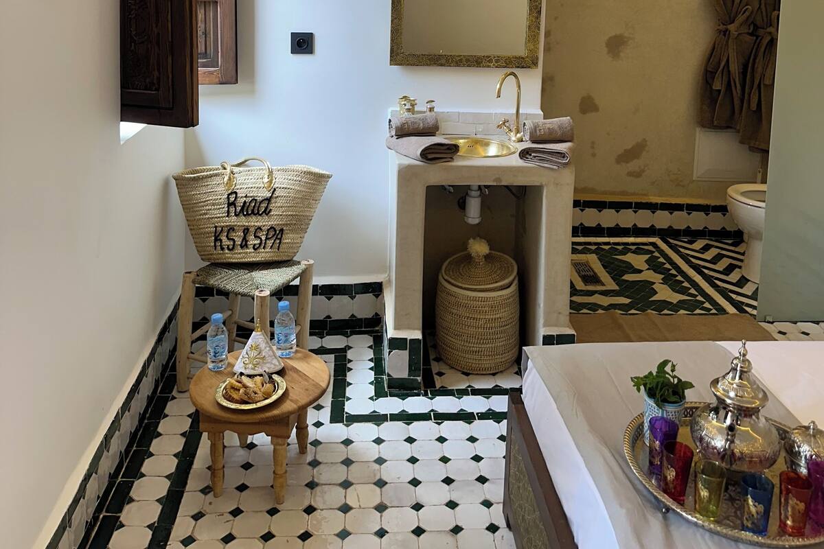 Une salle de bain avec un lavabo, un miroir et une douche. On y trouve un porte-serviettes et un tapis décoratif sur le sol.