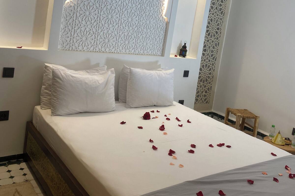 Un lit parfaitement fait, avec des draps blancs et des pétales de rose éparpillés sur la couverture.