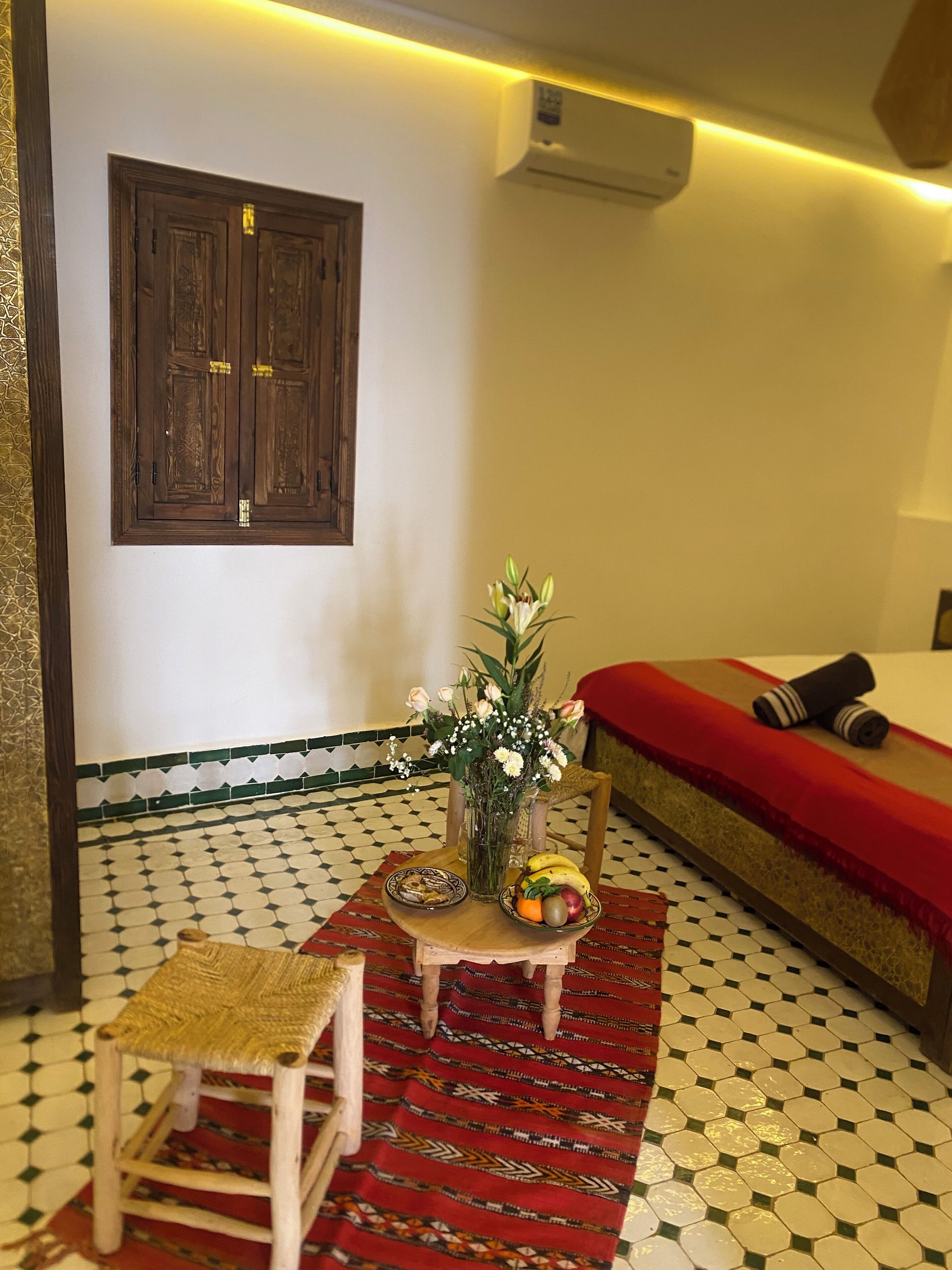 A room with a bed, a small table with a vase of flowers, a chair, and a patterned rug.