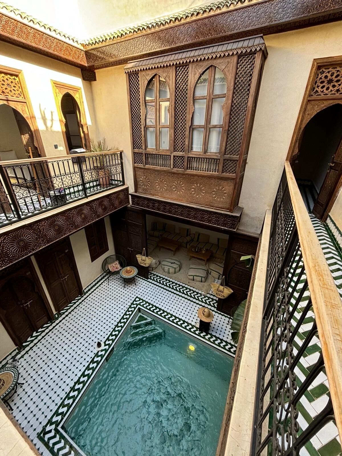 Un patio con piscina, mobiliario de madera y detalles arquitectónicos elaborados.