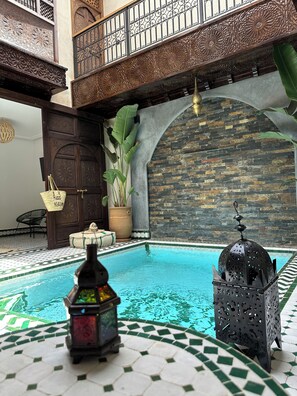 An indoor swimming pool with a tiled floor, surrounded by ornate wooden balconies and a stone wall. - RIAD KS & SPA (Marrakech)