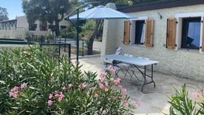 A patio area with a table and chairs, a blue umbrella, and pink flowers. - Apartement Avec Terrasse A 10 MN DES Plages A Pieds (LE LAVANDOU)