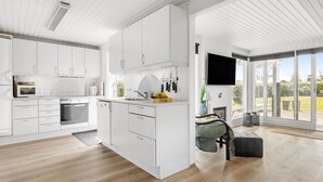 A modern kitchen with white cabinetry, a built-in oven, and a large window overlooking a garden. - 3 bedroom lovely home in Otterup (Otterup)