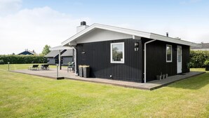 A modern black building with a number 57, a covered patio with outdoor furniture, and a well-maintained lawn. - 3 bedroom lovely home in Otterup (Otterup)