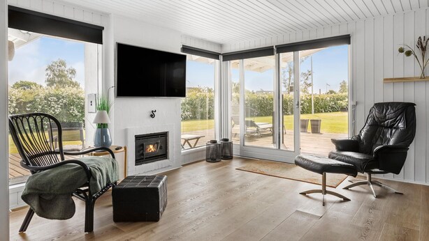 A modern living room with a fireplace, a flat-screen TV, and a view of the outdoors. - 3 bedroom lovely home in Otterup (Otterup)