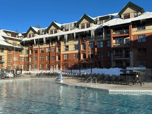 A hotel with a pool, snow-covered roofs, and a clear blue sky.