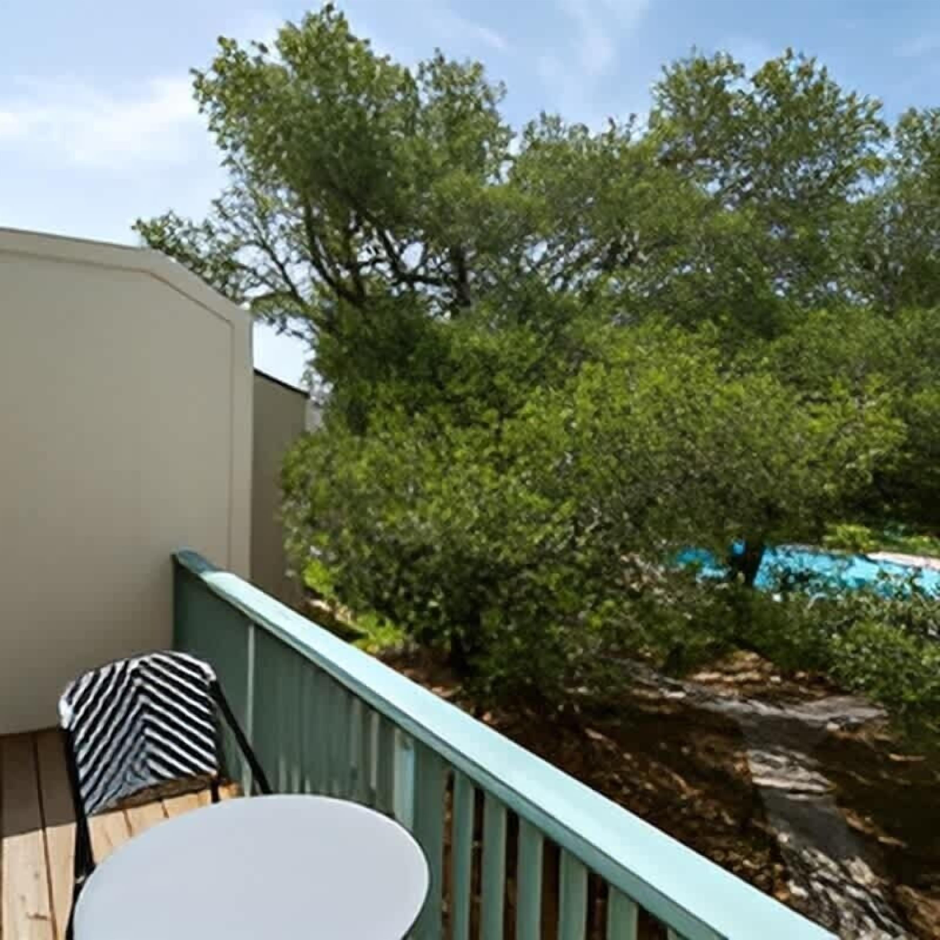 Un balcon avec une table blanche et une chaise à rayures, entouré de verdure et donnant sur une piscine.
