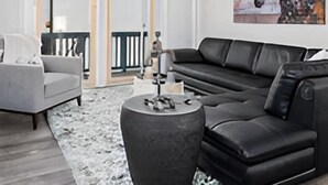 Un salon moderne avec un canapé en cuir noir, un fauteuil gris et une table basse ronde.