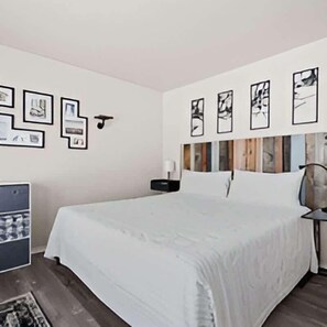 A bedroom with a bed, bedside table, wall-mounted artwork, and a small cabinet.