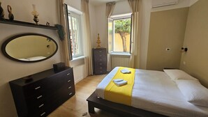 A bedroom with a bed, a dresser, a mirror, and a window with curtains. - 2 bedroom apartment in rome (Roma)