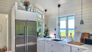 A modern kitchen with a stainless steel Bosch refrigerator, white cabinetry, a wooden countertop, and a view of the ocean through a large window.