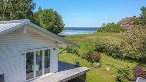 A white house with a deck overlooking a grassy area and a body of water.
