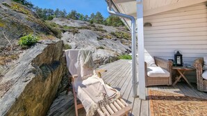 A wooden deck with a chair and a small table, overlooking a rocky landscape and a building with white siding.