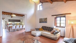 Una sala de estar con sofá, mesa de centro y un comedor con sillas, con una cocina al fondo.