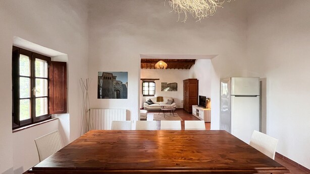 Un comedor con una mesa de madera y sillas blancas, un refrigerador blanco, y una cocina al fondo.