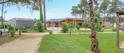 A building with a covered outdoor area, surrounded by a grassy lawn and trees.