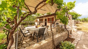 A covered outdoor dining area with stone flooring, a table with chairs, and a pergola with vines. - Beach front home in Novalja with house sea view (Novalja)